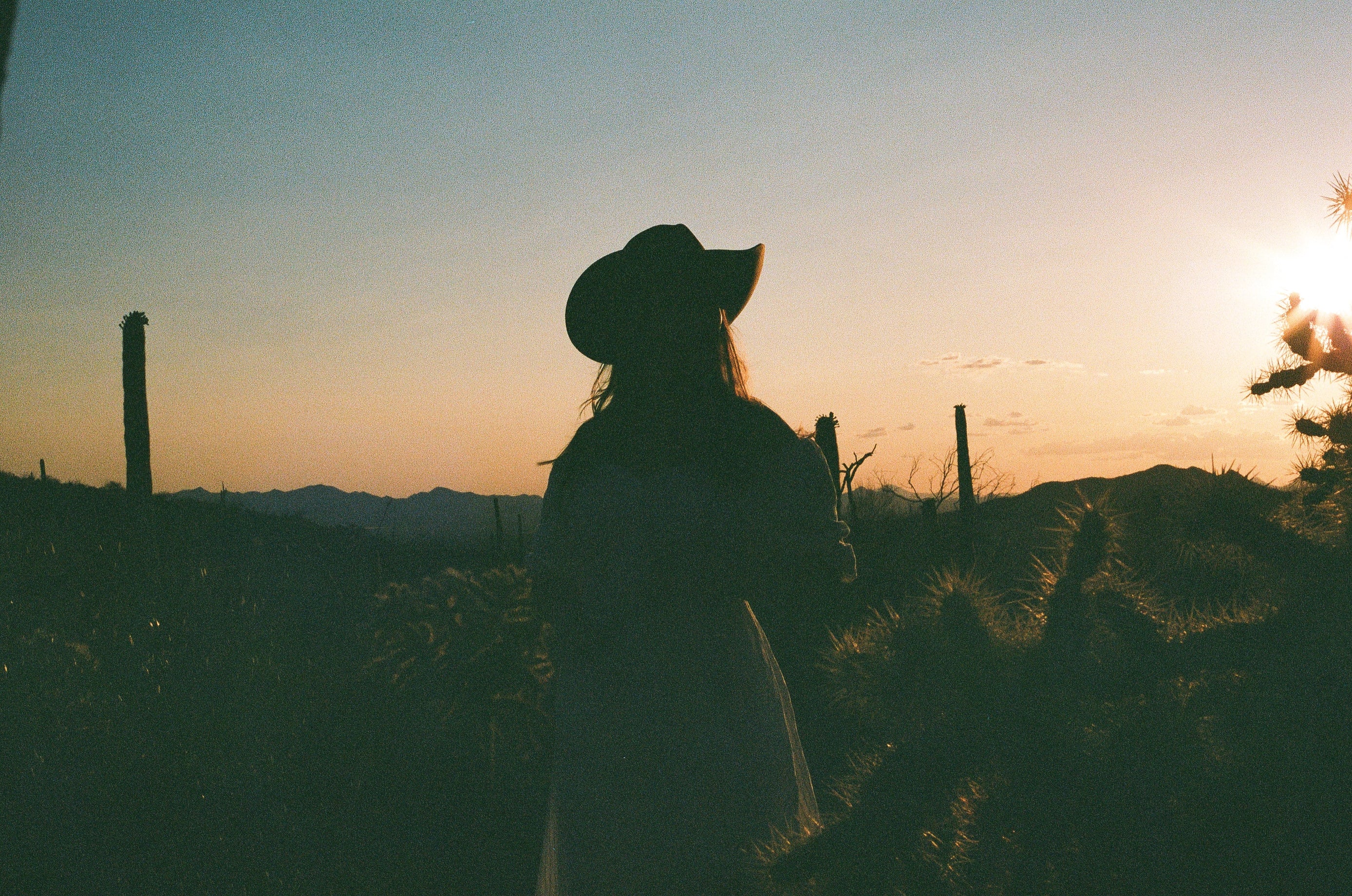 Woman standing in desert wearing cowboy hat at sunset