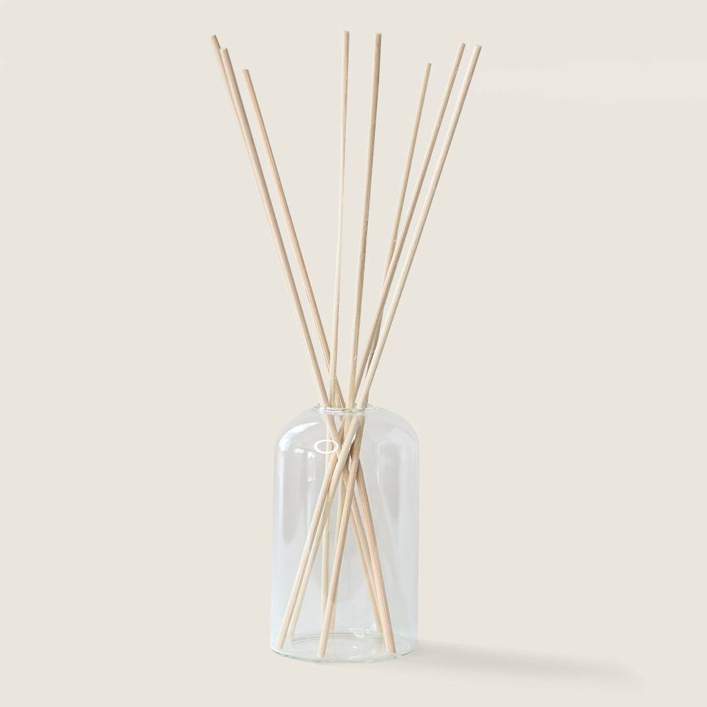 Clear glass diffuser bottle with wooden sticks on a light beige background