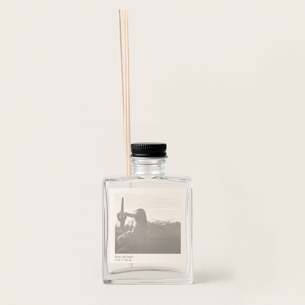 image of rectangular glass reed diffuser bottle with archival sepia toned image on front label. Bottle has black metal cap.