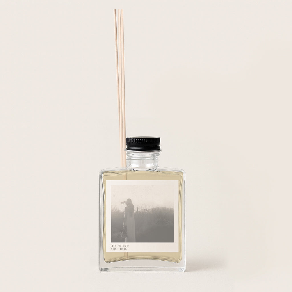 Image of rectangular glass reed diffuser bottle with archival sepia image on front label. Bottle has black metal cap.