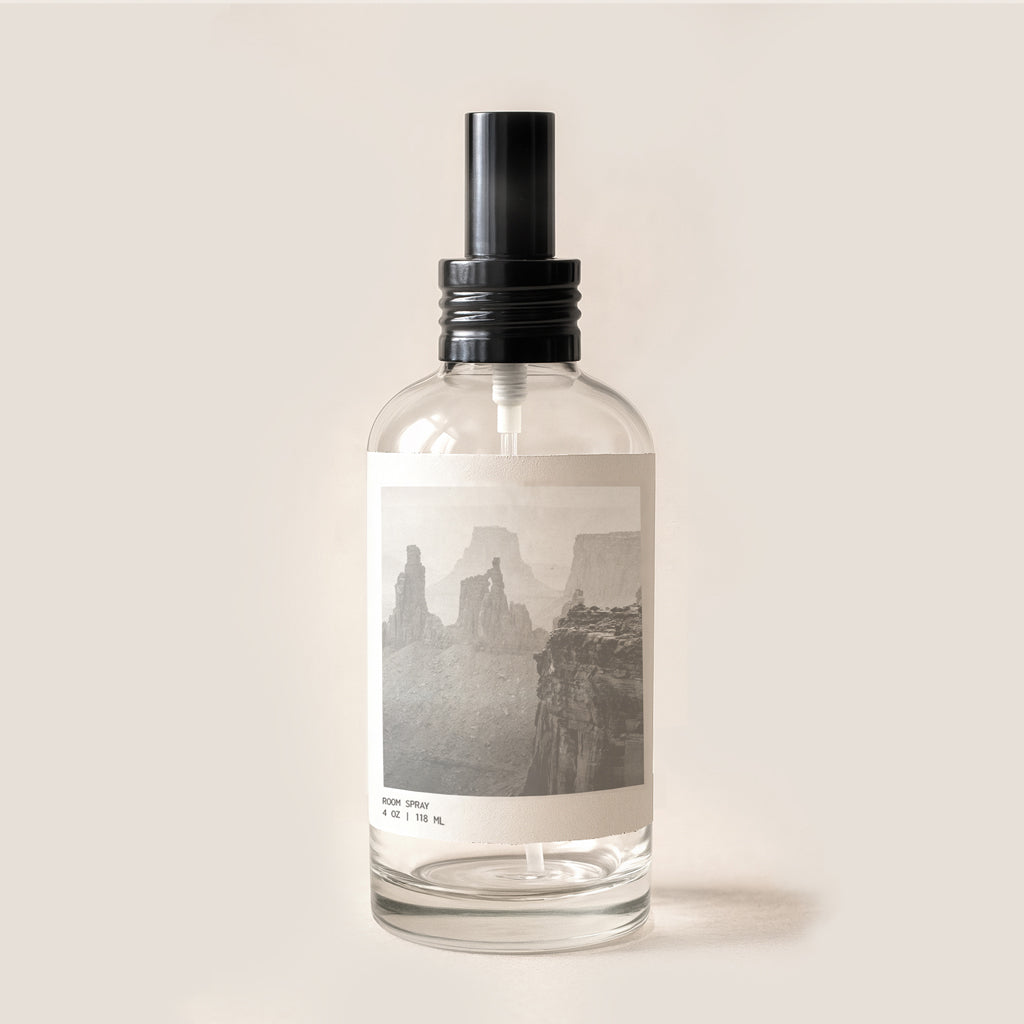 Image of glass bottle room spray with black metal cap. Bottle has archival canyon imagery on front label.