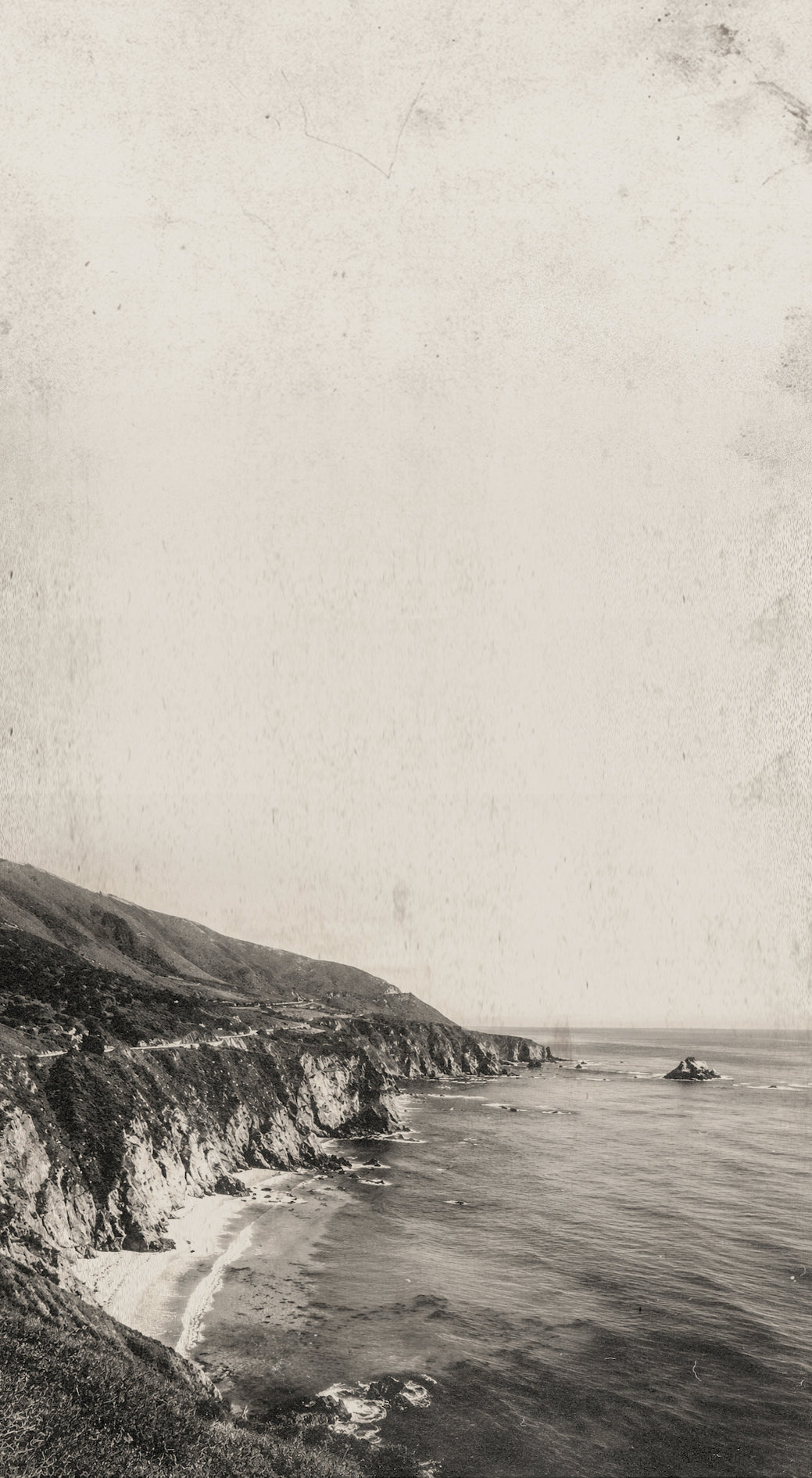 Vintage black and white coastal landscape photograph showing steep cliffs meeting the ocean under a pale sky, with a textured, aged paper appearance.