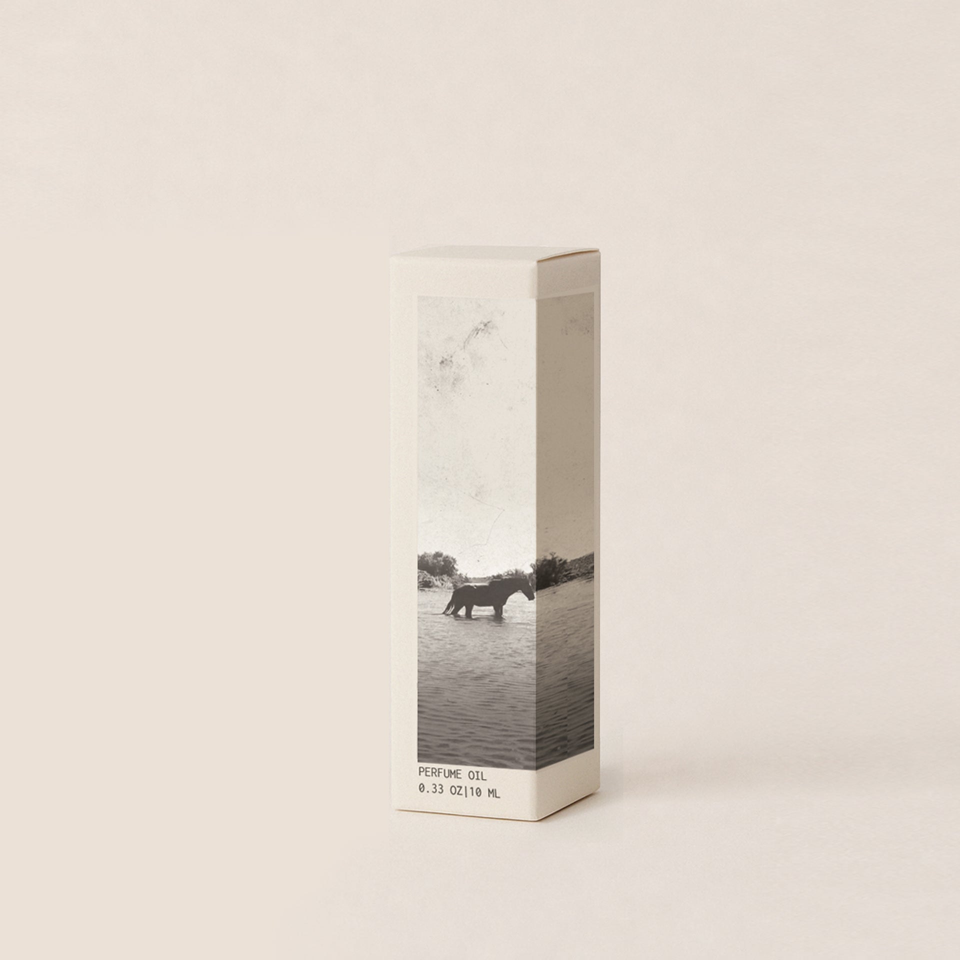 A off-white perfume box with a grayscale photographic print of an horse walking through water, standing on a light beige background.