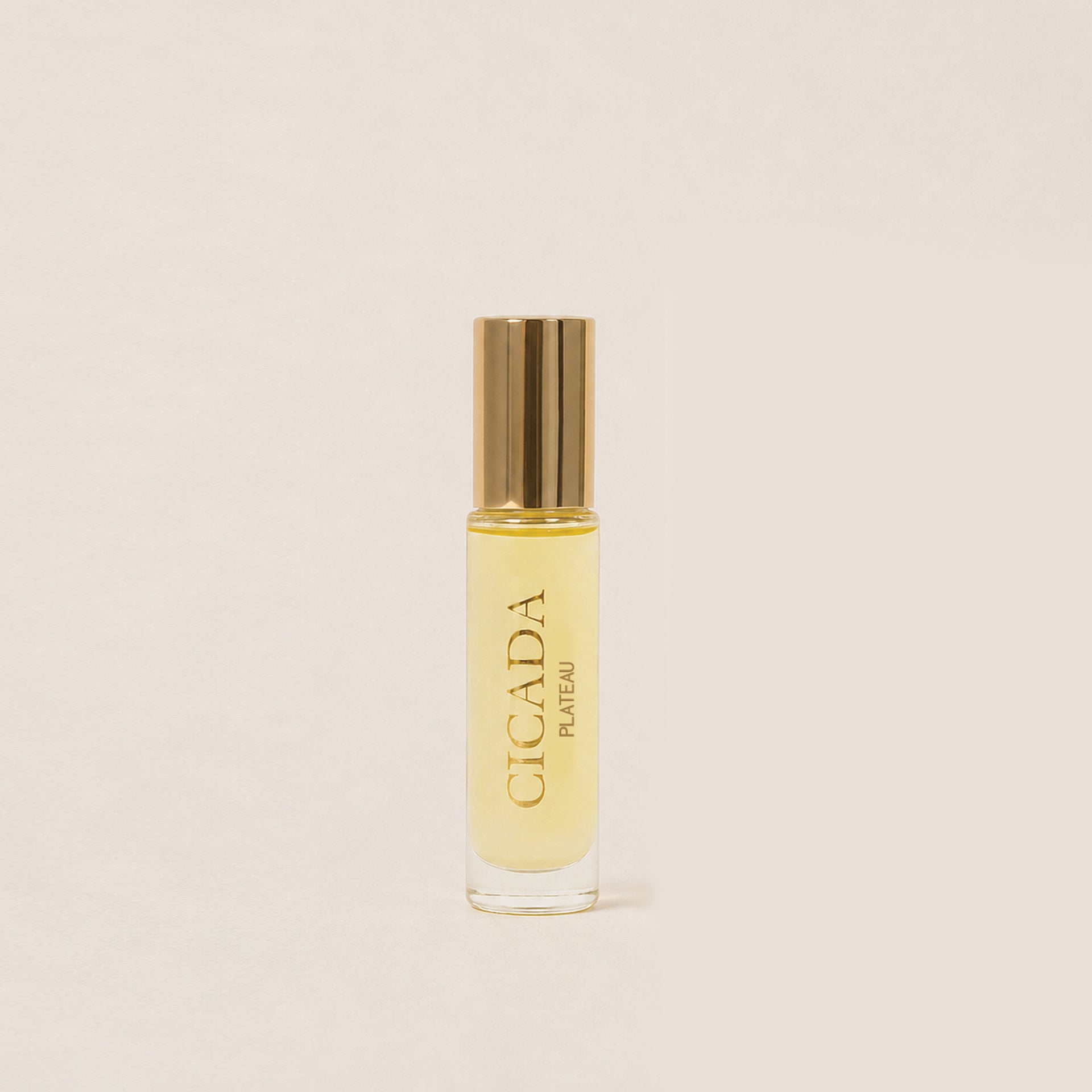A small clear glass perfume oil bottle and a shiny gold cap, standing upright on a warm off-white background. The bottle is labeled 'CICADA PLATEAU'.