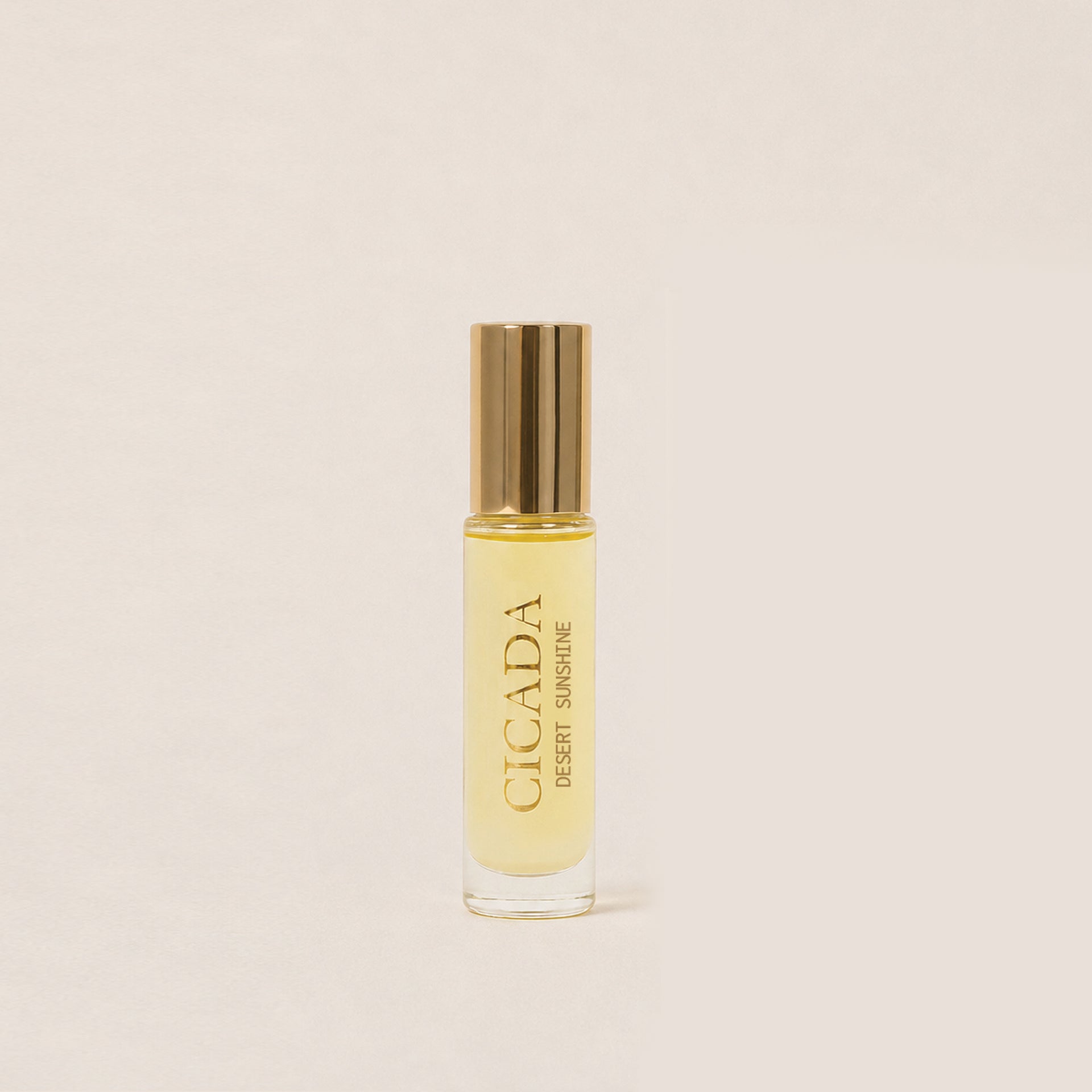 CICADA glass perfume oil bottle with a metallic gold cap and gold CICADA lettering, set against a solid light beige background.