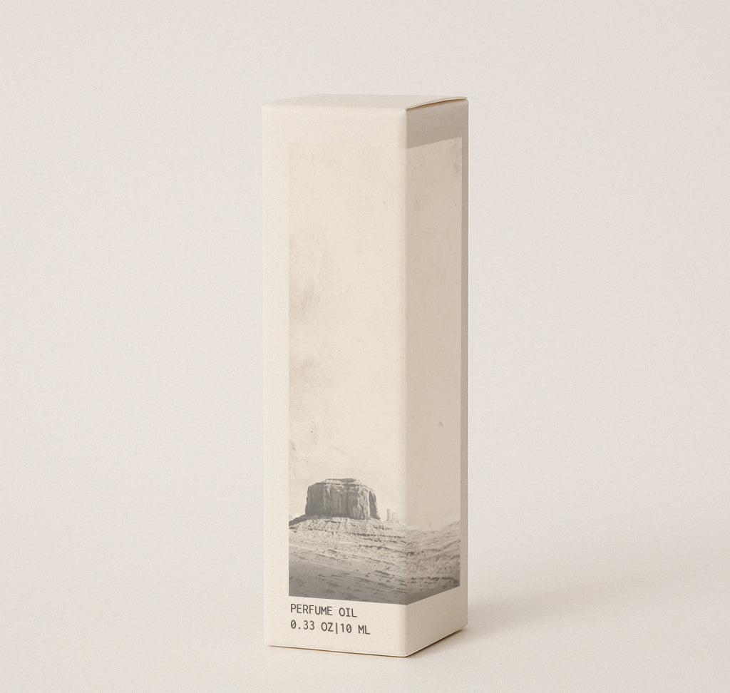 Product image of box that perfume oil comes in. Box measures 1" wide x 1" deep x 4" high. Box is light cream colored with desert image on it with the text 'Perfume oil' and ' 0.33oz | 10 ml'. Image has cream colored background. 