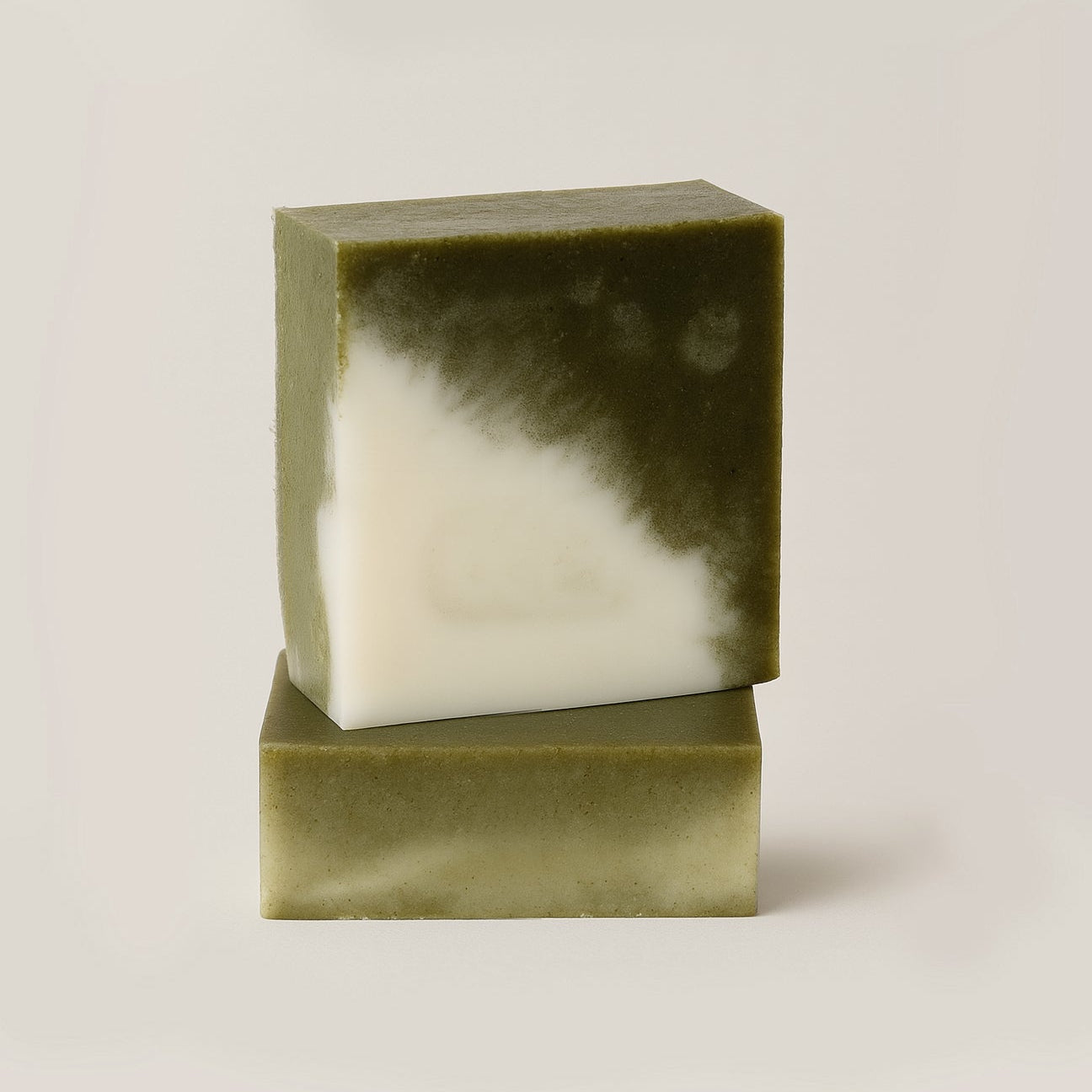 Two green bars of soap stacked on a light beige background